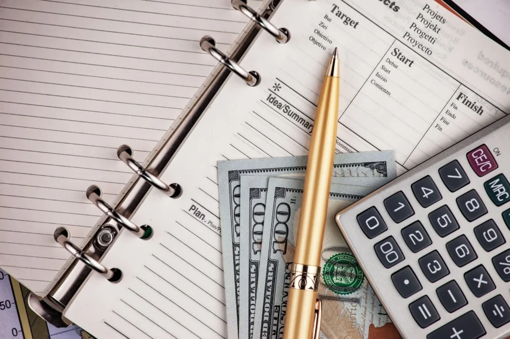 Finance agenda open, with a gold pen, dollar bills and a calculator.