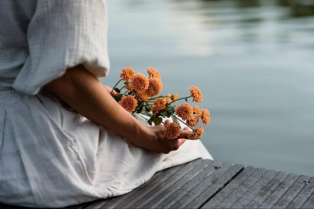 Woman grabbing flowers in front of a lake.