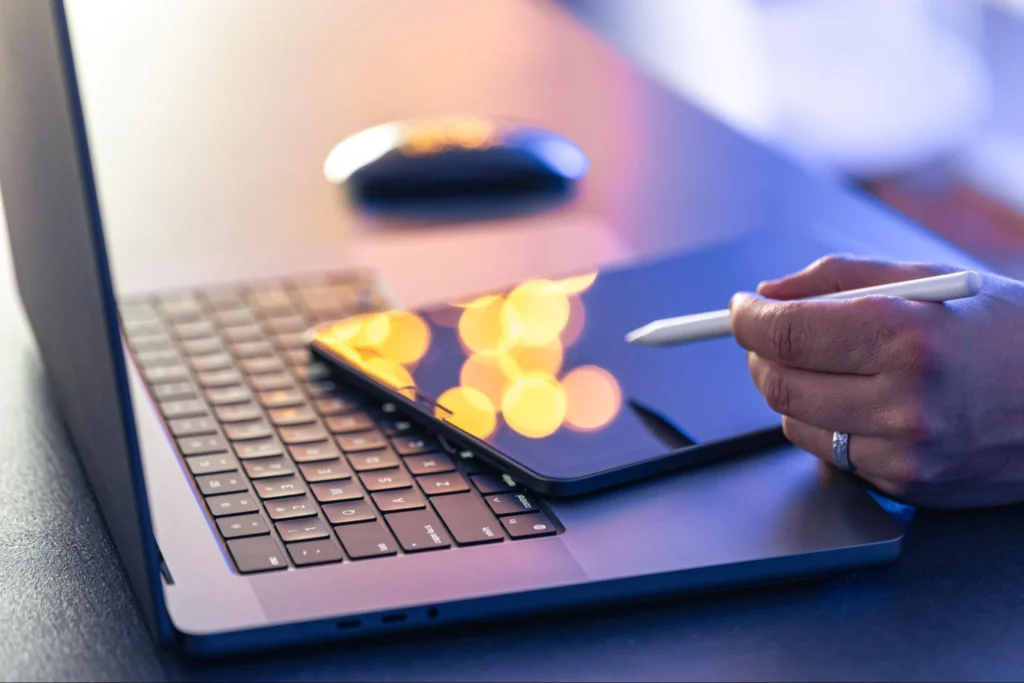 A tablet with a pencil being hold by a person.